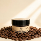 A jar of Velafora Coffee Honey Sugar Scrub sits on a bed of roasted coffee beans against a warm beige background with soft diagonal shadows.