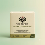 A square cardboard box of Velafora Neem & Tea Tree Soap, 85 gm, shown against a soft mint green gradient background. The box is cream-colored with dark green text and a botanical logo, and features a dark green band at the bottom.