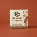 A rectangular box of Velafora Loofah Soap centered against a solid terracotta background. The box is cream-colored with brown text and illustrations of loofah leaves and a loofah fruit.

