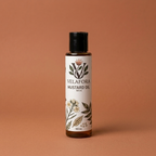 A 100 ml bottle of Velafora Mustard Oil with a black cap and a white botanical label, set against a solid terracotta background.