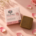 Velafora Glowing Soap bar next to its pink and white floral box, styled on a pink surface with scattered rose petals.