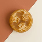 A round, textured amber-brown loofah sponge or decorative stone piece, photographed from above on a diagonally split terracotta and off-white background.

